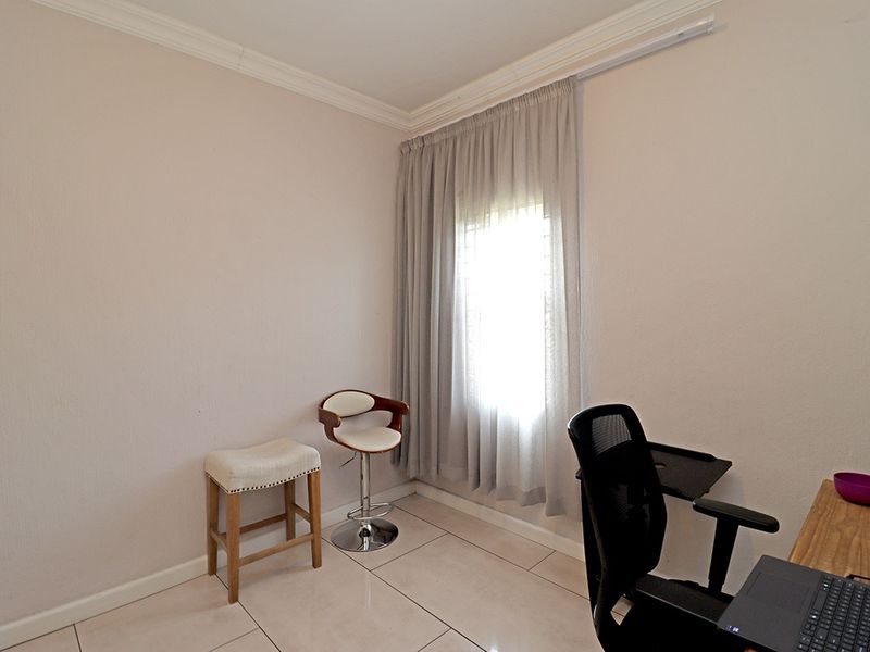 A functional bedroom space featuring neutral tiled flooring, cornice detailing, and a window fitted with a curtain rail.
