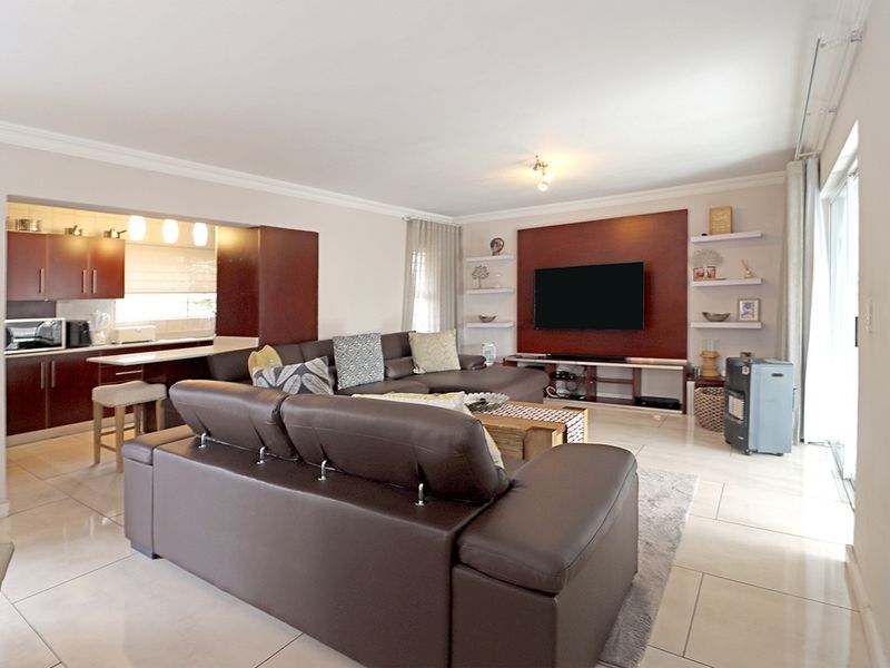 Spacious open-plan living area featuring a modern kitchen with breakfast bar, tiled floors, and a custom built-in media wall with floating shelving.