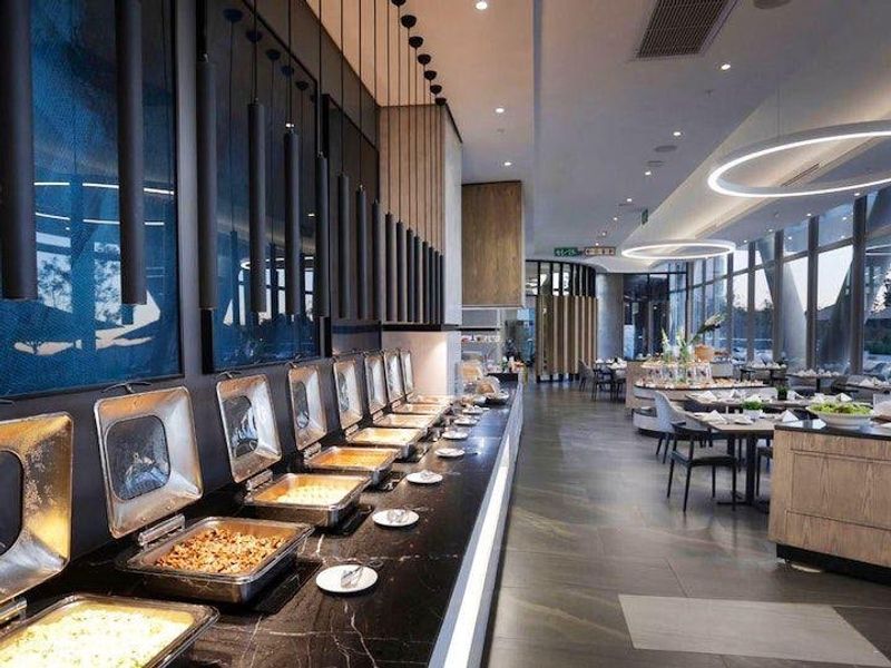 Modern clubhouse dining area featuring a sleek black marble buffet station, contemporary pendant lighting, and expansive floor-to-ceiling windows.