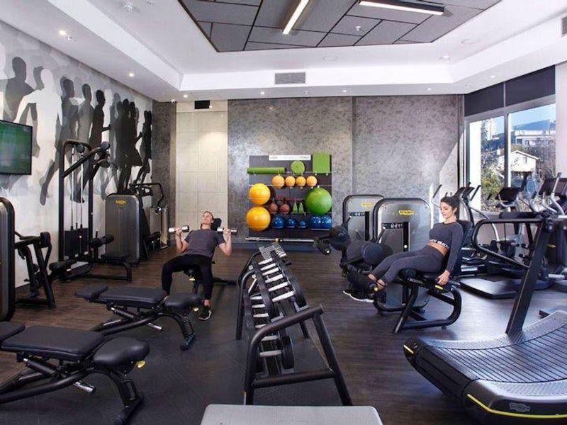 A modern, well-equipped apartment complex gym featuring high-quality flooring, recessed ceiling lighting, and large glass doors providing natural light.