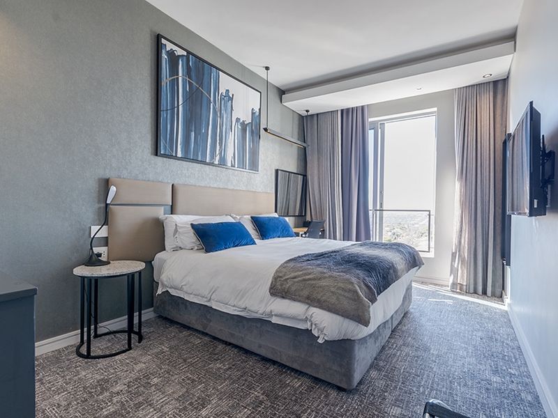 A modern, well-appointed bedroom featuring textured wallpaper, recessed ceiling lighting, and direct access to a private balcony with expansive views.