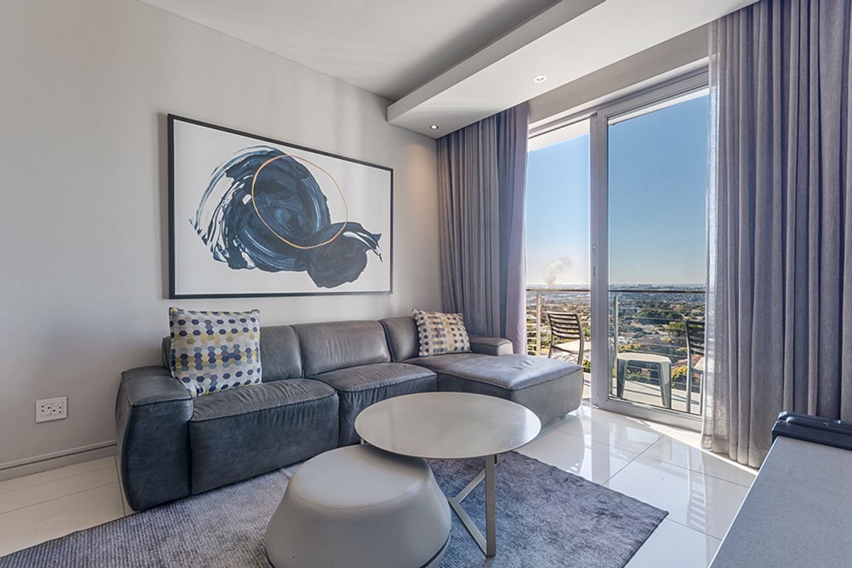 Modern living room featuring sleek tiled floors, recessed ceiling lighting, and a large sliding glass door providing access to a balcony with expansive views.
