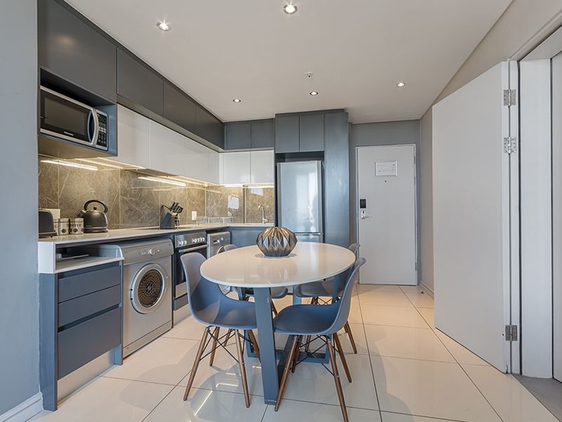 Modern open-plan kitchen featuring sleek two-tone cabinetry, stone-look backsplash, integrated appliances, and polished tiled flooring in a contemporary apartment setting.