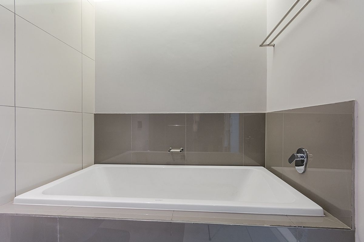 A clean, modern bathroom featuring a built-in bathtub with neutral-toned wall tiles and chrome fixtures.