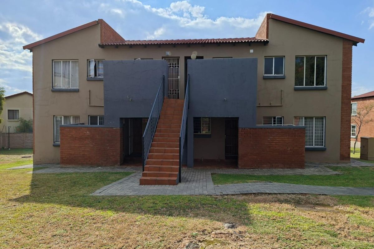 Rear view of a two-story apartment building featuring a central external staircase, brick accents, and paved access paths within a communal garden area.