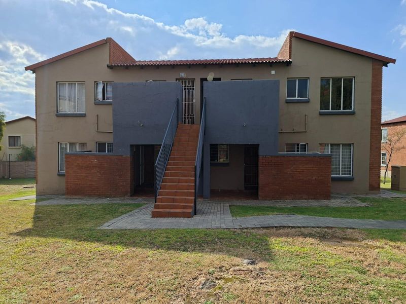Rear view of a two-story apartment building featuring a central external staircase, brick accents, and paved access paths within a communal garden area.