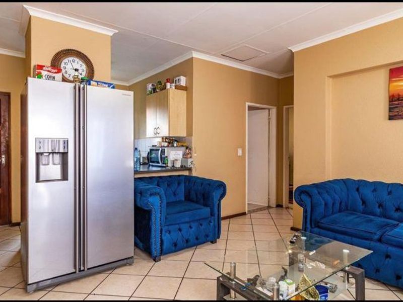 Open-plan living area featuring tiled flooring and coved ceilings, seamlessly connecting the living space with a compact kitchen area.
