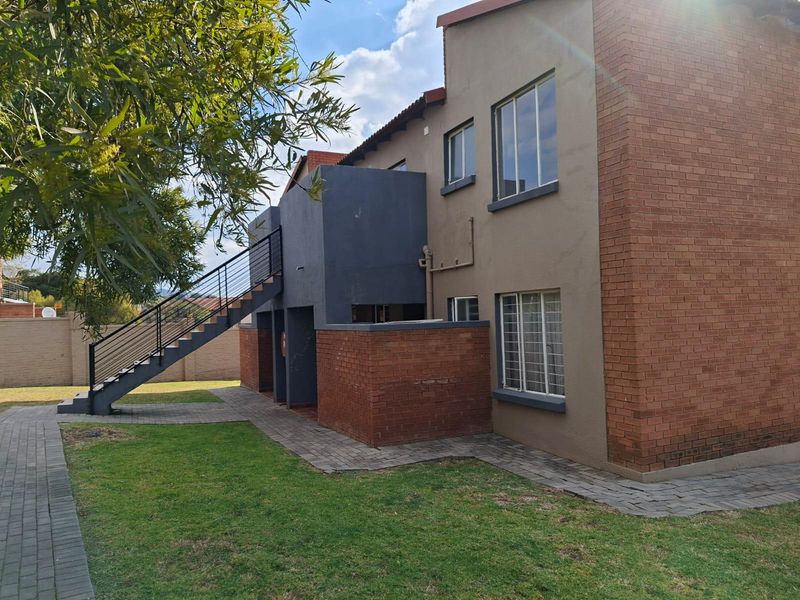 Rear view of a multi-story apartment building featuring a brick and rendered facade, external staircase, and paved garden pathways.