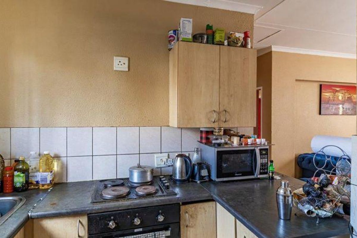 A compact kitchen featuring laminate cabinetry, a built-in electric hob and oven, and a tiled splashback, offering a functional layout for an apartment.