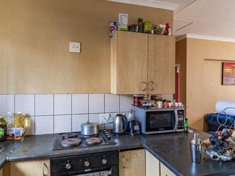 A compact kitchen featuring laminate cabinetry, a built-in electric hob and oven, and a tiled splashback, offering a functional layout for an apartment.