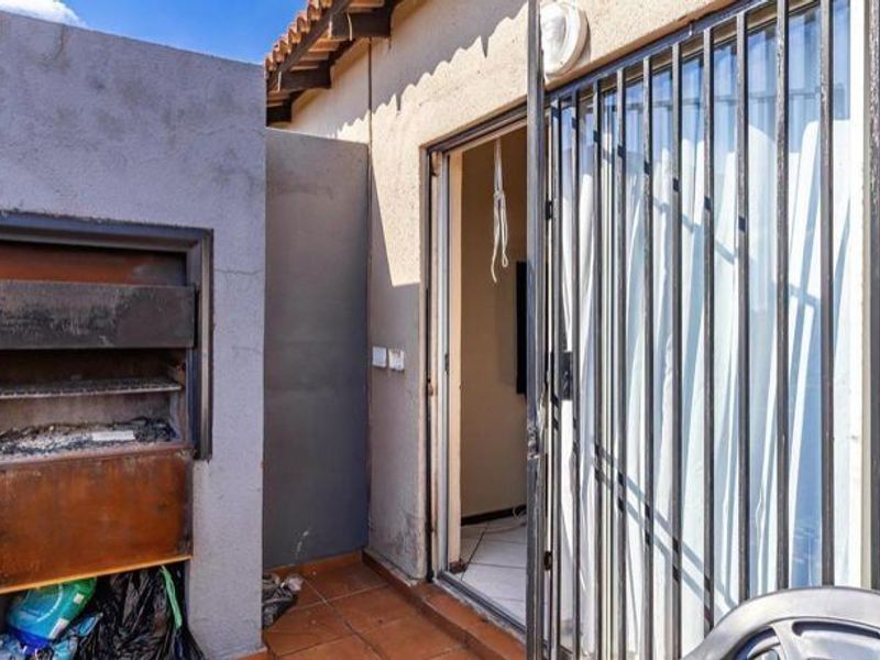 Outdoor patio area featuring a built-in braai, tiled flooring, and a security gate providing access to the interior living space.