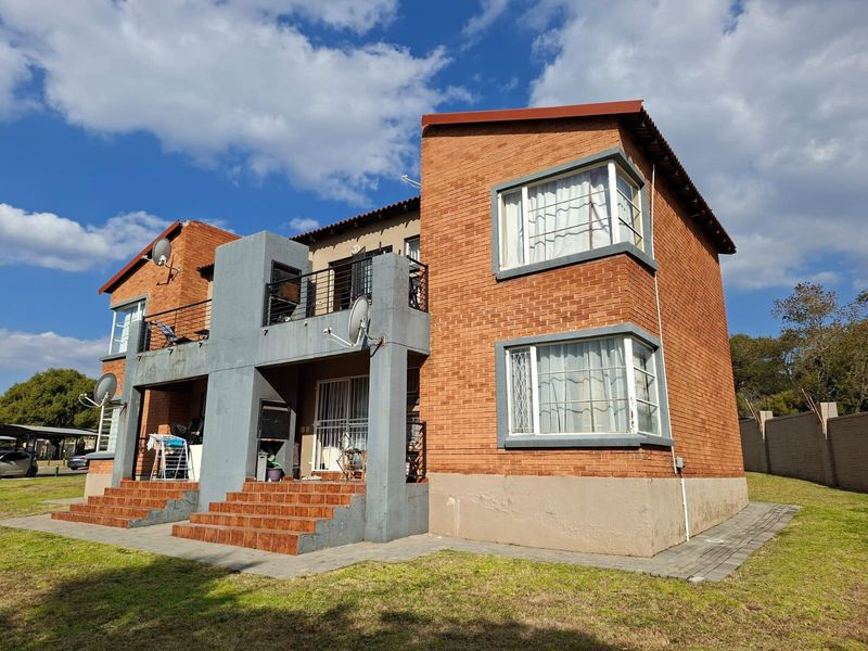 Exterior view of a two-story face brick apartment building featuring corner windows, tiled entrance steps, and a balcony with metal railings.