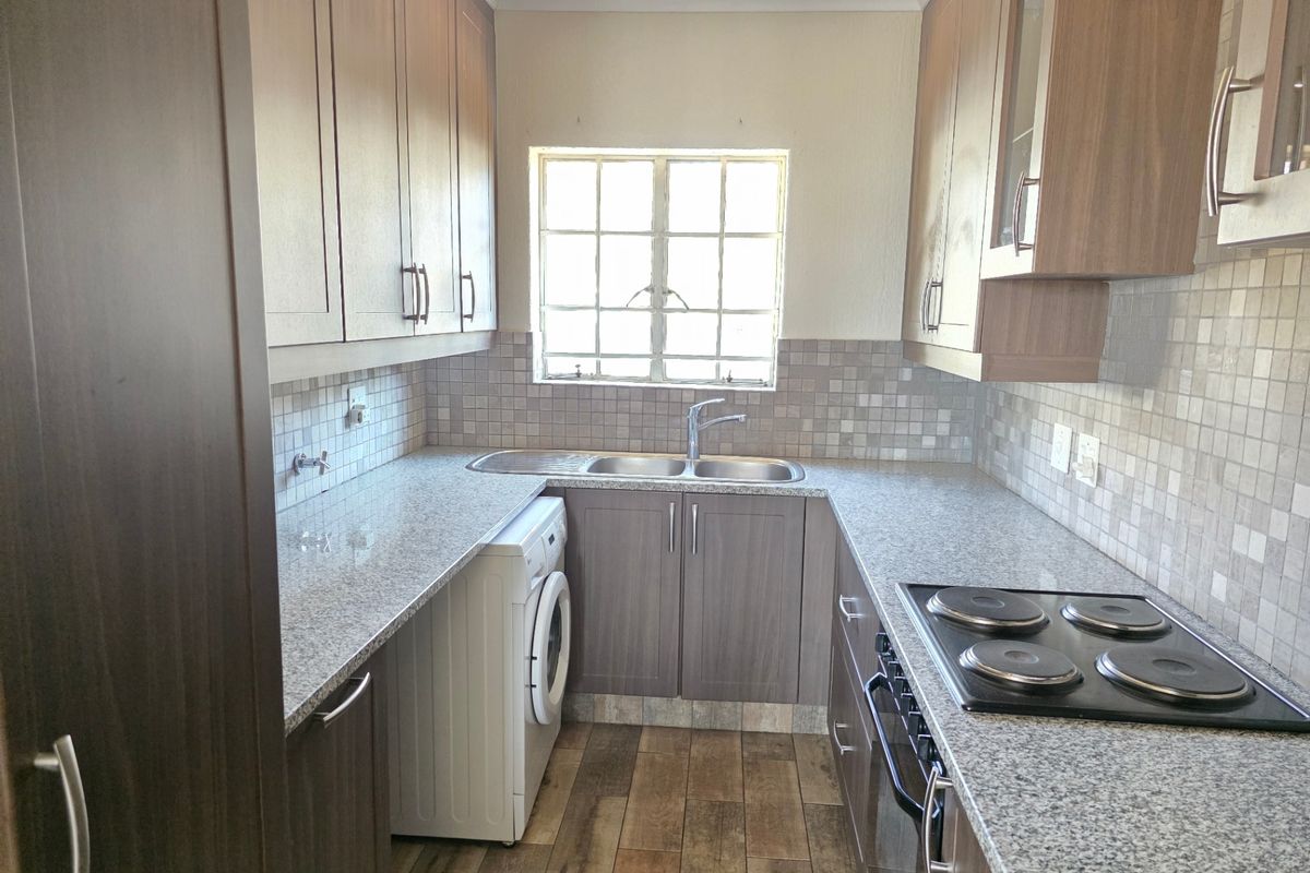 A functional galley-style kitchen featuring wood-finish cabinetry, granite countertops, a mosaic tile backsplash, and integrated electric cooking appliances.