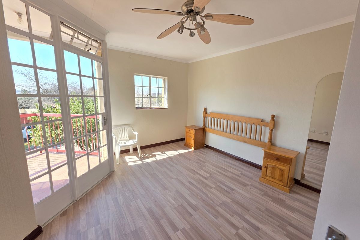 A bright bedroom featuring laminate flooring, a ceiling fan, and large french doors providing access to an outdoor balcony area.