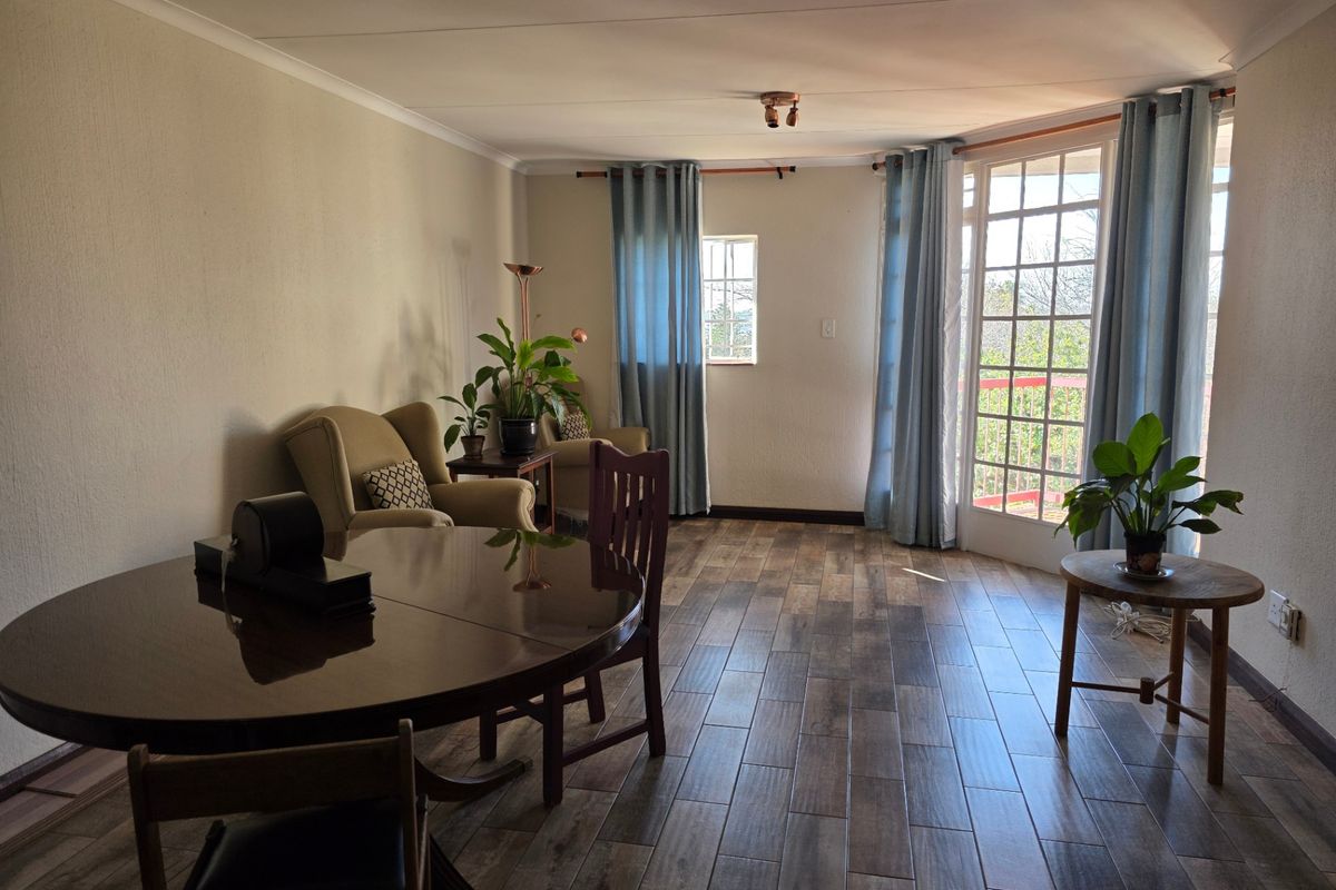 A living area featuring wood-look tile flooring, coved ceilings, and access to an outdoor balcony through classic french doors.