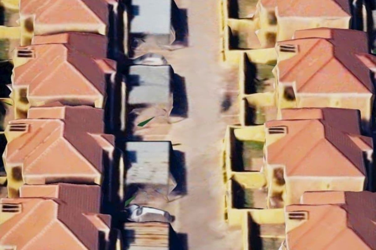 An aerial view of a townhouse complex featuring rows of units with tiled roofs and a central paved driveway.