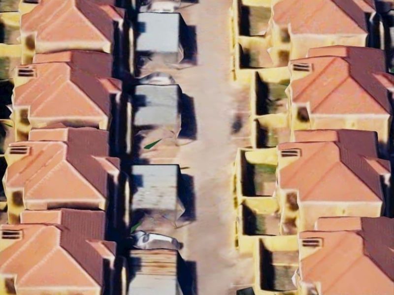 An aerial view of a townhouse complex featuring rows of units with tiled roofs and a central paved driveway.