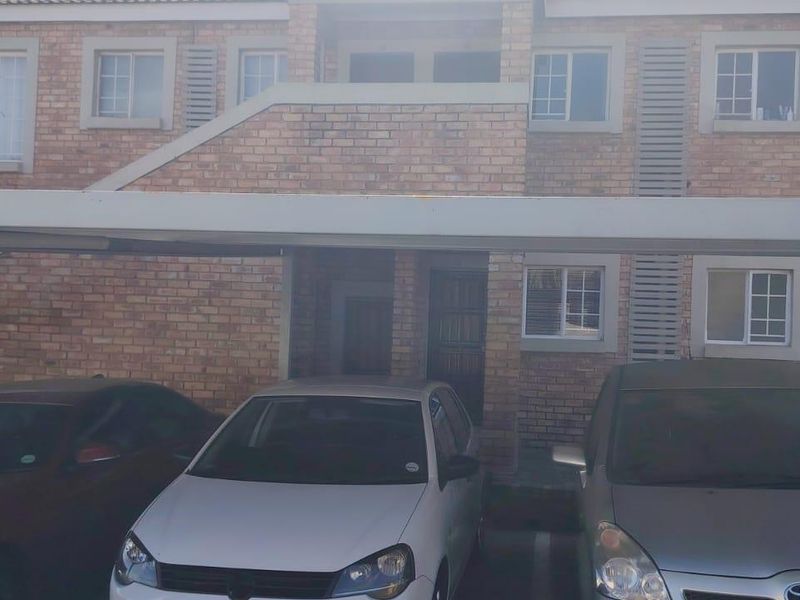 Front elevation of a face brick townhouse featuring a covered carport and multiple casement windows.