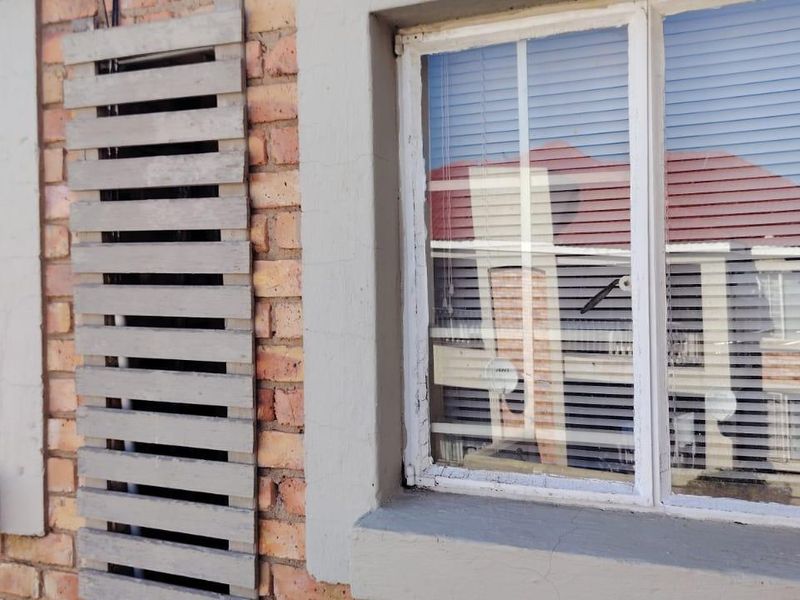 Close-up view of the townhouse exterior featuring face brick walls, decorative timber screening, and window frames requiring maintenance.