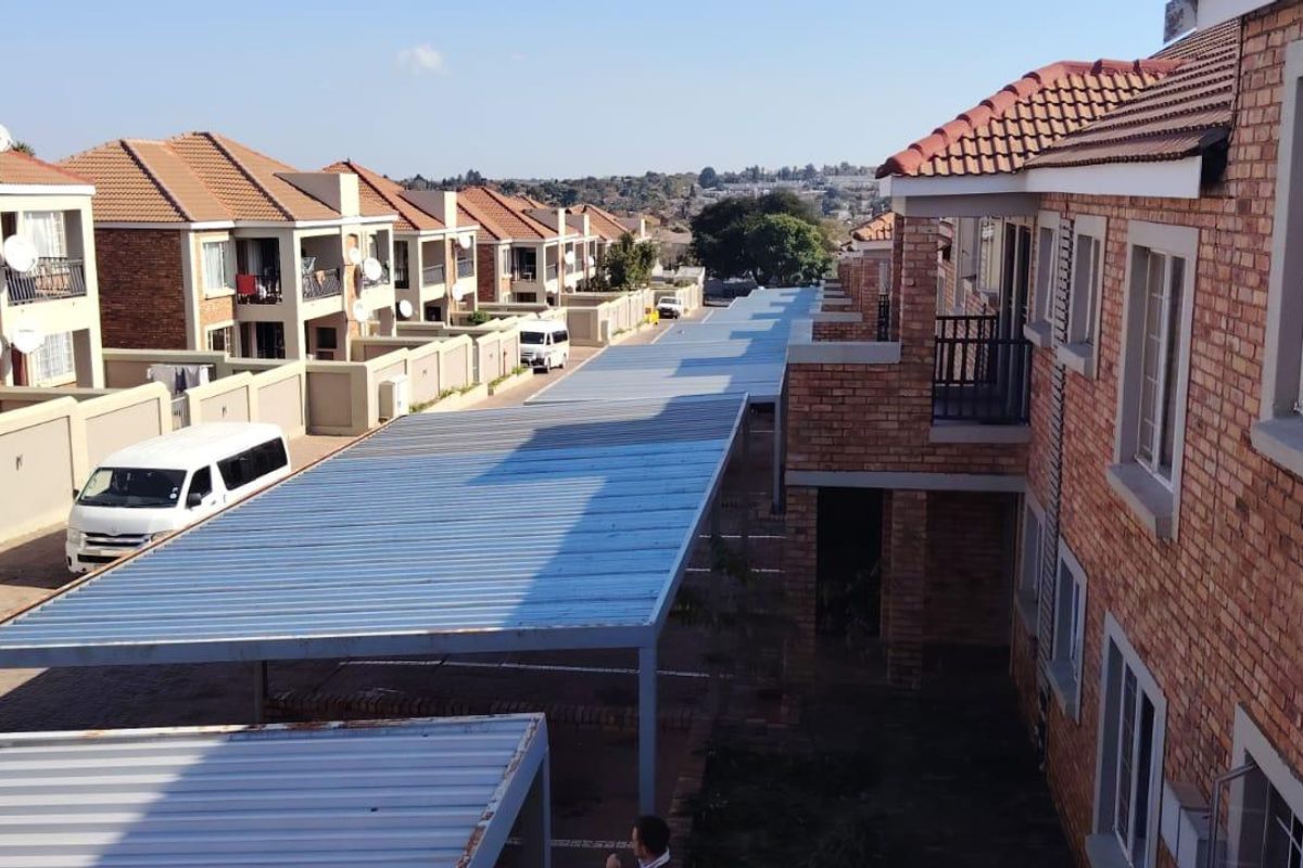 An elevated view of a townhouse complex featuring brick facades, tiled roofs, and covered parking carports within a residential estate setting.