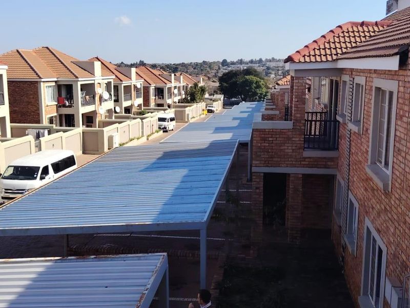 An elevated view of a townhouse complex featuring brick facades, tiled roofs, and covered parking carports within a residential estate setting.