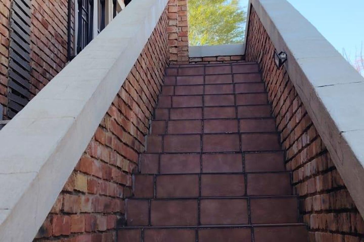 An exterior view of a brick staircase leading to the entrance of the townhouse, featuring tiled steps and concrete balustrades.