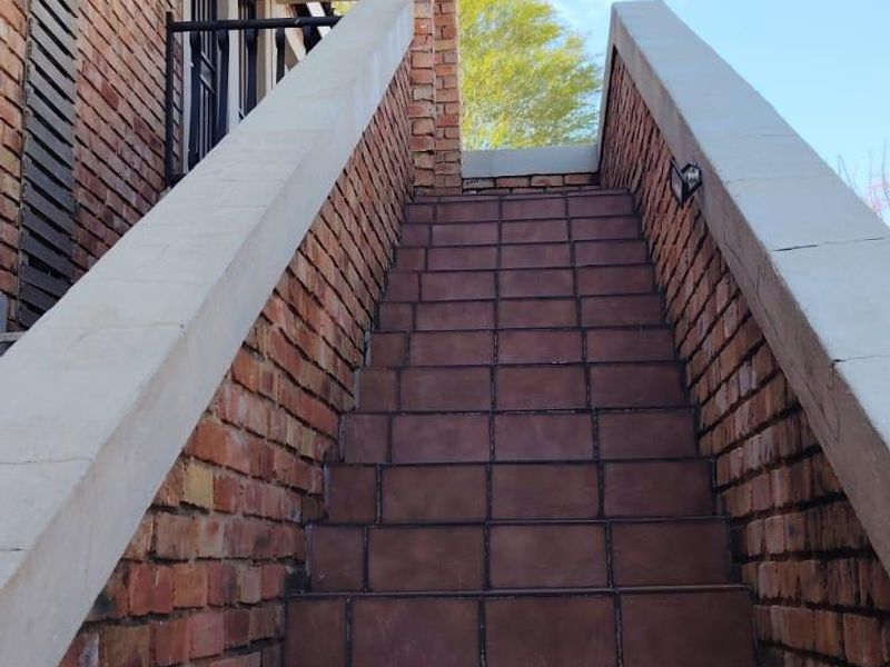 An exterior view of a brick staircase leading to the entrance of the townhouse, featuring tiled steps and concrete balustrades.