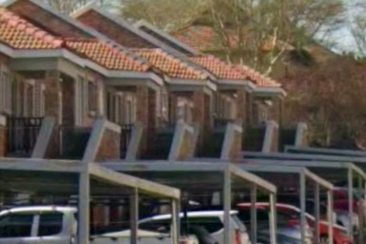 Exterior view of a townhouse complex featuring a row of units with tiled roofs and dedicated carport parking bays.