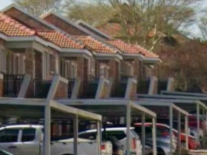 Exterior view of a townhouse complex featuring a row of units with tiled roofs and dedicated carport parking bays.