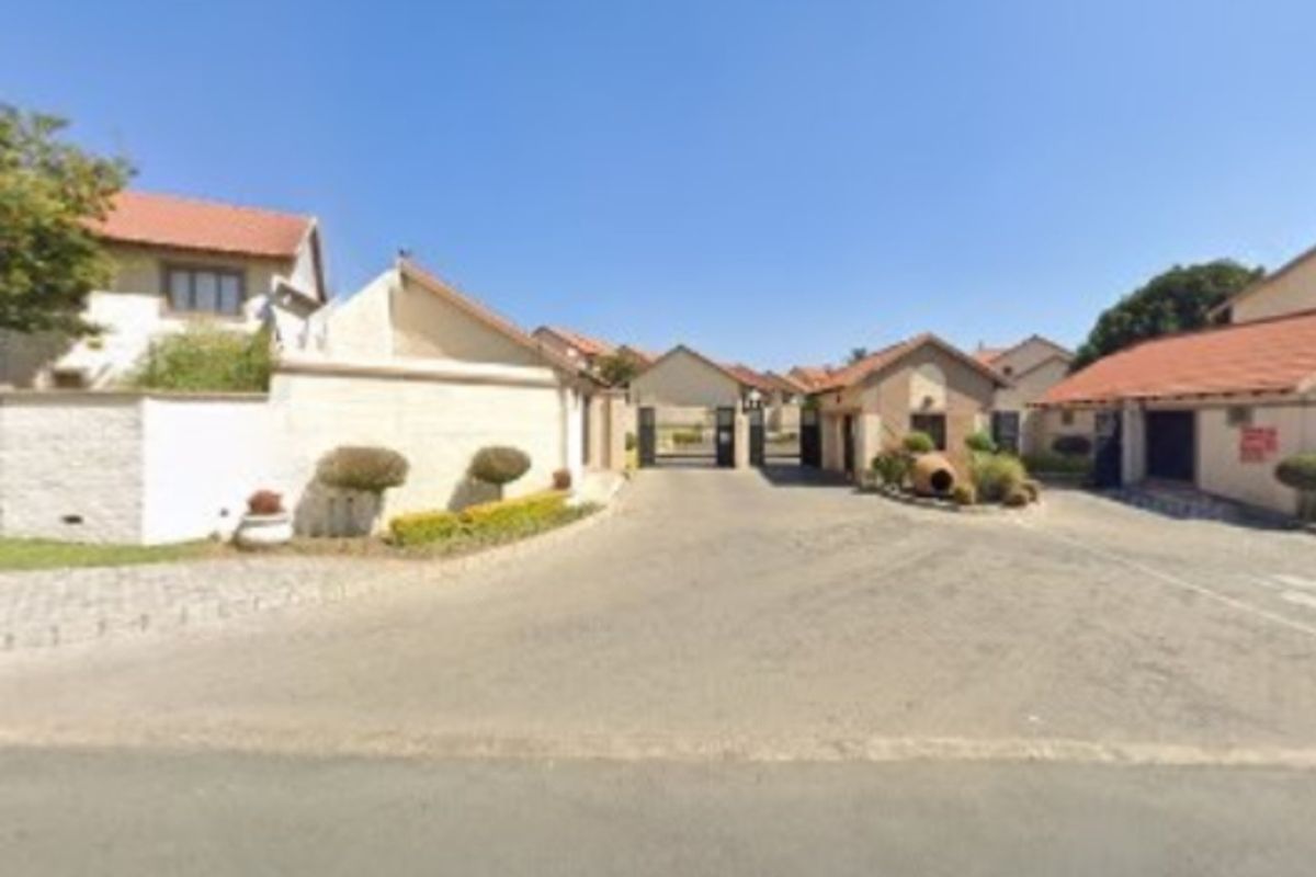 View of the gated entrance and security access point for the townhouse complex, featuring paved driveways and established perimeter walls.