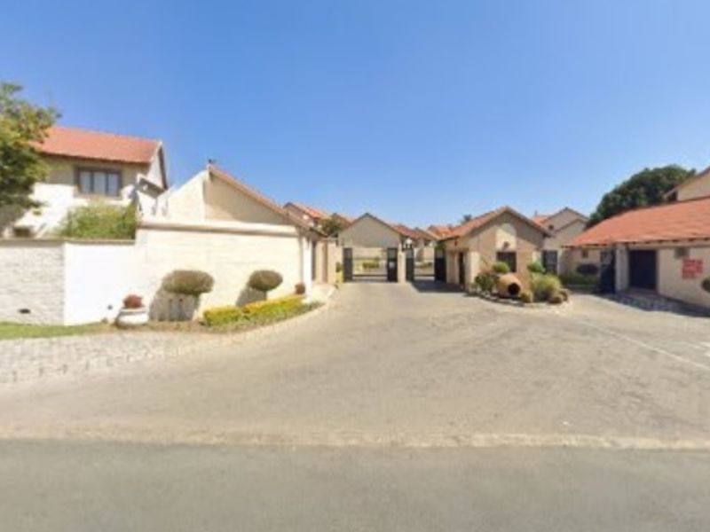 View of the gated entrance and security access point for the townhouse complex, featuring paved driveways and established perimeter walls.