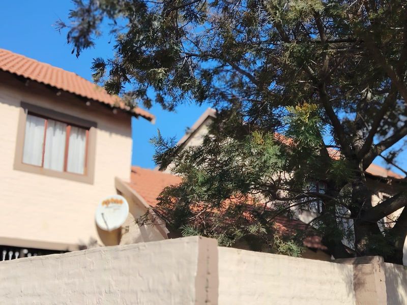 A view of the townhouse exterior featuring terracotta roof tiles, a boundary wall, and a mounted satellite dish.