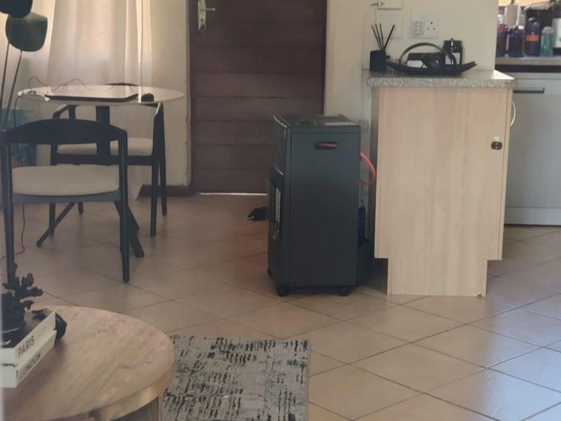 Open plan living area featuring tiled flooring and a functional kitchen corner with laminate countertops and wooden door access.