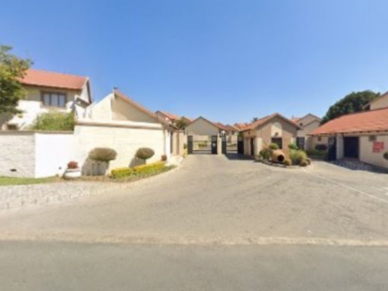 View of the secure entrance and driveway leading into the townhouse complex, featuring perimeter walls and tiled roof structures.