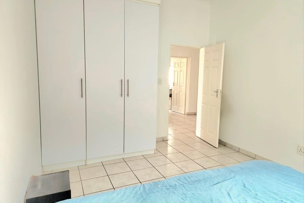 A bedroom featuring white built-in cupboards and tiled flooring, with an open doorway leading to an adjacent hallway.