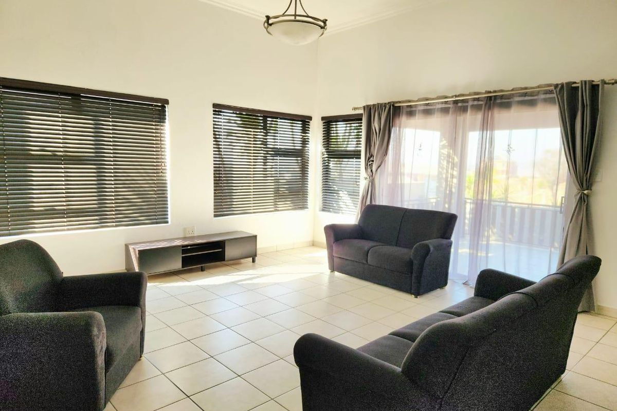 A bright and spacious living room featuring neutral tiled flooring, large windows with venetian blinds, and sliding door access to an outdoor area.
