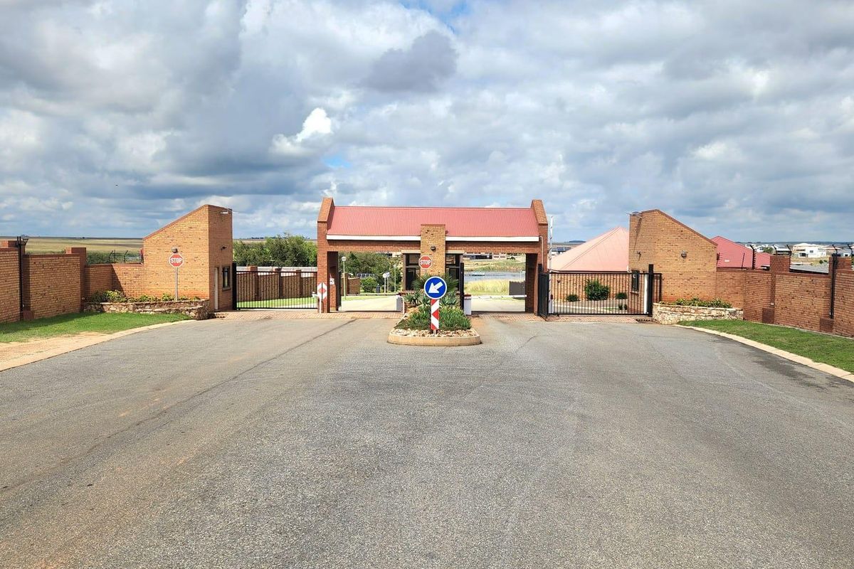 A secure gated entrance to the residential estate featuring brick pillars, metal security gates, and a paved driveway approach.