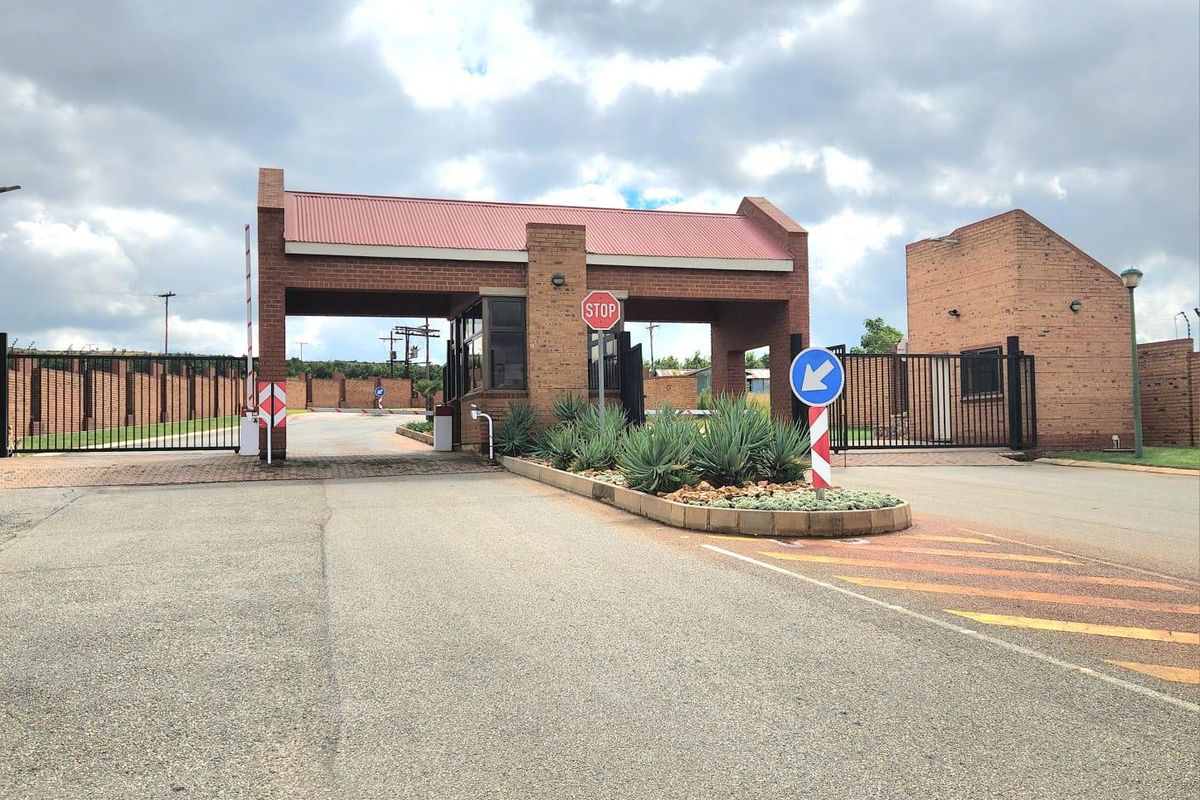 Secure gated entrance to the residential estate featuring brick guardhouse, automated boom gates, and perimeter fencing.