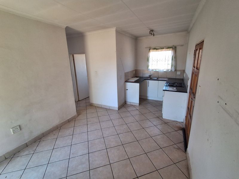 An open-plan living and kitchen area featuring tiled flooring, basic cabinetry, and a built-in hob, offering a blank canvas for renovation.