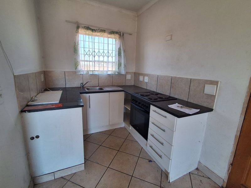 Compact kitchen featuring built-in cabinetry, laminate countertops, integrated oven and hob, and tiled flooring. Requires cosmetic updates to improve overall appeal.