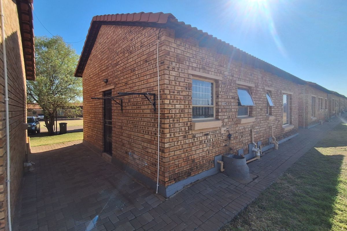 Rear view of the townhouse featuring face brick construction, tiled roof, paved walkway, and external plumbing fixtures.