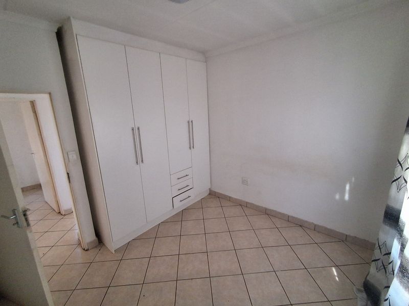 A clean, empty bedroom featuring neutral ceramic floor tiles and white built-in cupboards, offering a versatile space ready for personalization.