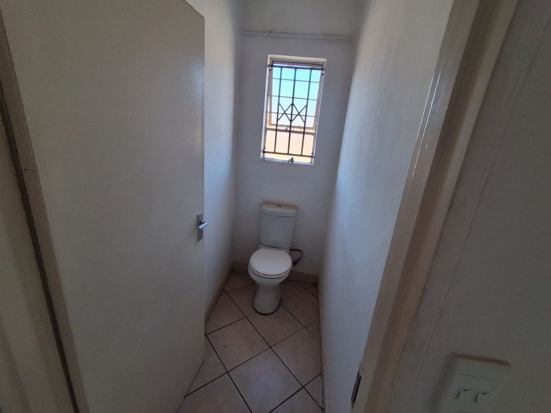 A compact, empty guest toilet featuring tiled flooring and a small window with a security gate.