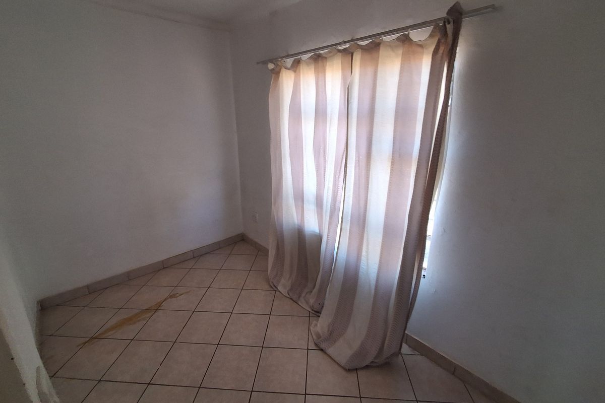 An empty bedroom featuring tiled flooring and a curtain rod, requiring minor cosmetic attention to address floor staining.