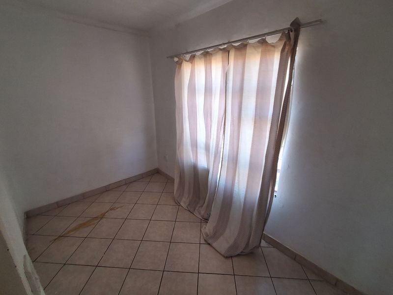 An empty bedroom featuring tiled flooring and a curtain rod, requiring minor cosmetic attention to address floor staining.