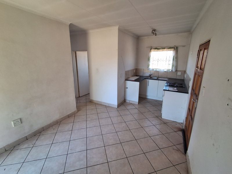 An empty kitchen featuring tiled flooring, built-in cabinetry, and a hob, offering a functional space ready for renovation or personalization.