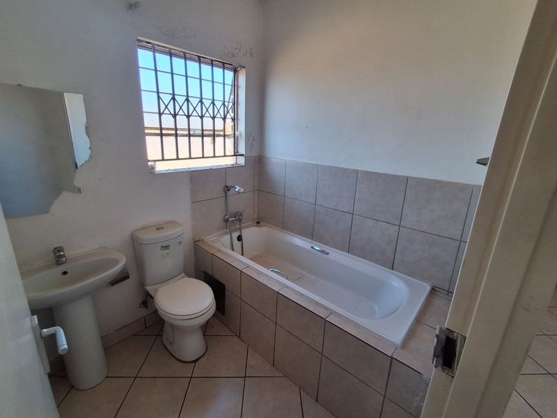 A functional bathroom featuring a pedestal basin, toilet, and tiled bathtub with security bars on the window, requiring cosmetic updates.