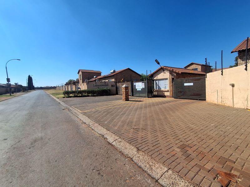 Street view of the townhouse complex entrance featuring brick paved parking, perimeter walling, and secure gated access.