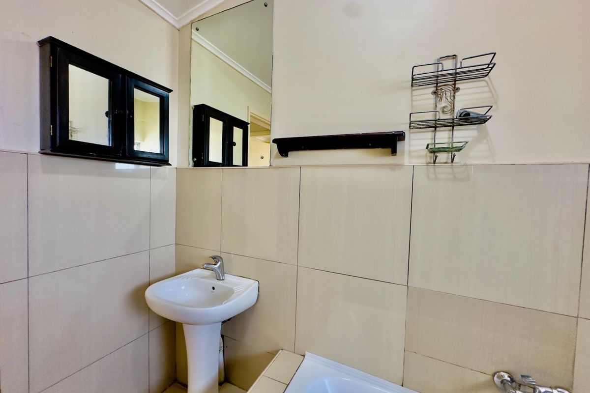 A functional bathroom featuring a pedestal basin, built-in bathtub, and wall-mounted mirror with neutral tiled walls.