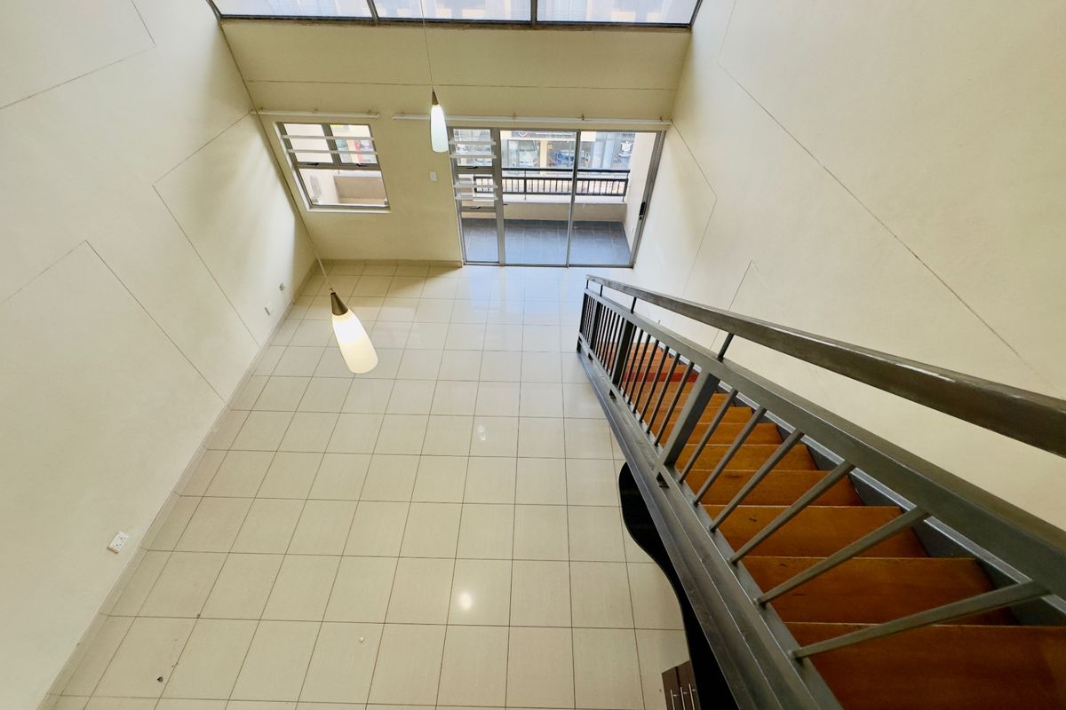 Spacious double-volume living area featuring tiled floors, a staircase with metal railings, a skylight, and access to a private balcony.